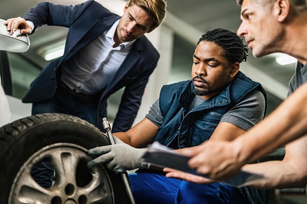 Mecânico afro-americano e seu colega de trabalho consertando um pneu do carro do cliente na oficina de automóveis