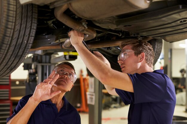 Mecánico y aprendiz masculino trabajando juntos debajo del automóvil