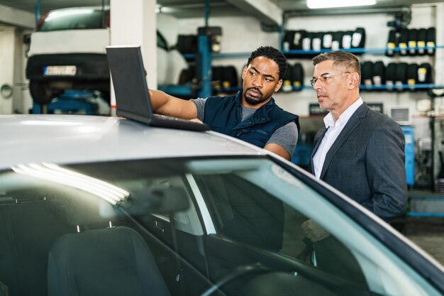 Mecánico de automóviles afroamericano y su gerente usando una computadora en un taller de reparación