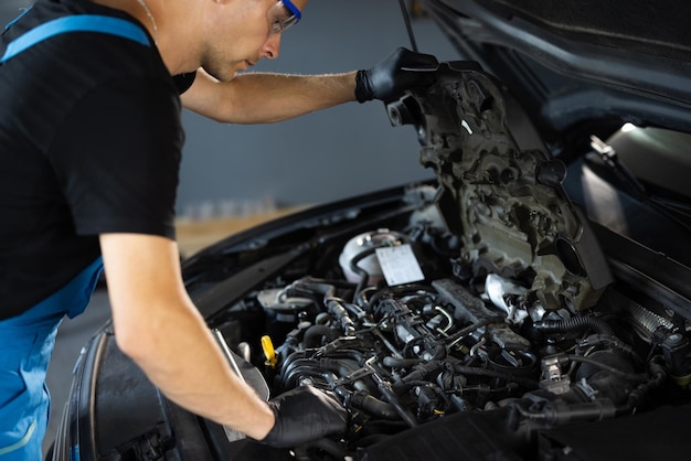 Mecánico de automóviles anotando piezas de reparación durante la reparación del motor del capó del automóvil abierto en el garaje