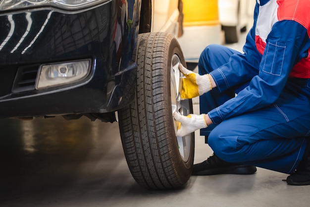 El mecánico de automóviles asiático está quitando la rueda y revisando los frenos y la suspensión en el servicio del automóvil con una carretilla elevadora. Centro de reparacion y mantenimiento