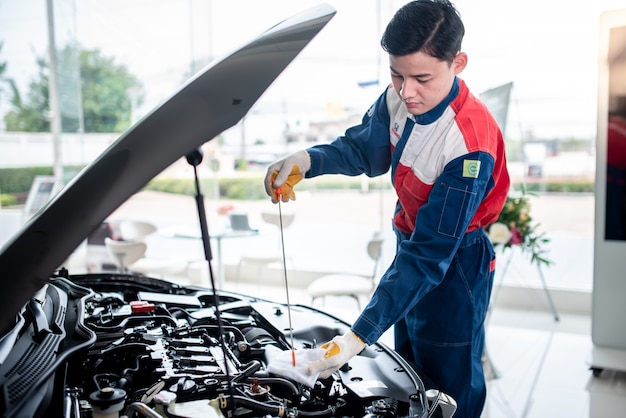 Un mecánico de automóviles asiático en un taller de reparación de automóviles está revisando el motor. Para los clientes que usan automóviles para servicios de reparación, el mecánico trabajará en el garaje.