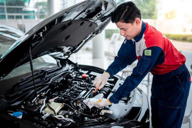 Un mecánico de automóviles asiático en un taller de reparación de automóviles está revisando el motor. Para los clientes que usan automóviles para servicios de reparación, el mecánico trabajará en el garaje.