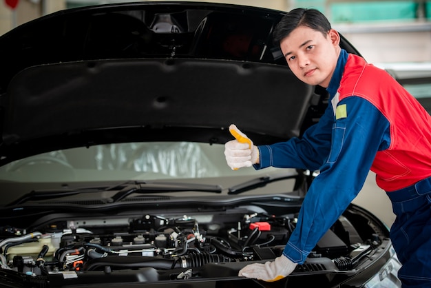 Un mecánico de automóviles asiático en un taller de reparación de automóviles está revisando el motor. Para los clientes que usan automóviles para servicios de reparación, el mecánico trabajará en el garaje.