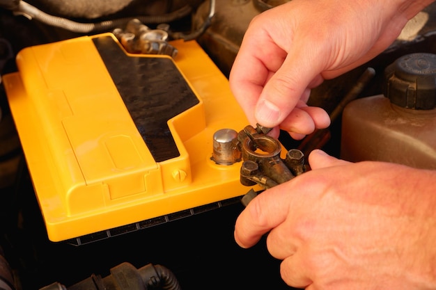 Un mecánico de automóviles cambia la batería en un automóvil Un electricista de automóviles conecta la terminal a una nueva batería Vista de primer plano