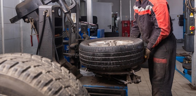 Mecánico de automóviles cambiando el neumático en la llanta en el garaje de servicio