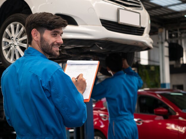 Mecánico de automóviles caucásico en uniforme con portapapeles de orden de servicio trabajando en garaje. Lista de verificación del técnico para reparar la máquina de un automóvil en el garaje.