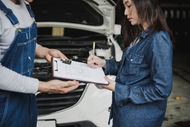 Mecánico de automóviles confiable que muestra el portapapeles a una clienta.