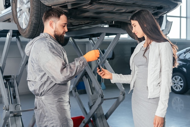 Mecánico de automóviles dando las llaves del coche a su clienta en el taller de calidad del centro de reparación de automóviles