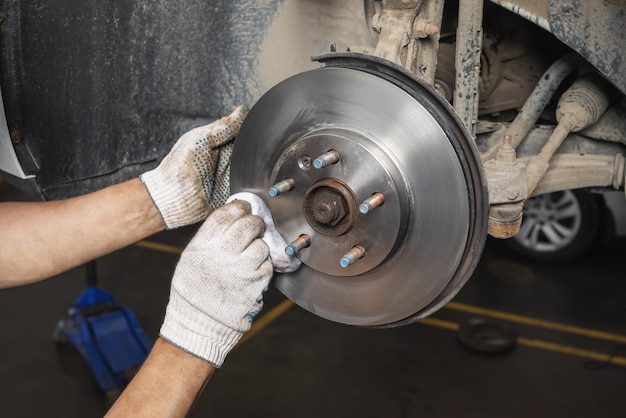 Un mecánico de automóviles elimina la suciedad y los residuos de grasa de un disco de freno de coche recién instalado con un pañuelo