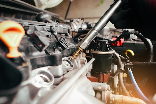 Un mecánico de automóviles está instalando bujías de iridio para automóviles en el enchufe de chispa de encendido del bloque del motor en el compartimiento del motor con herramientas específicas