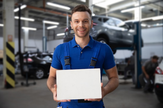 Mecánico de automóviles guapo con la pizarra en blanco en la mano está planteando contra el moderno servicio de reparación de automóviles