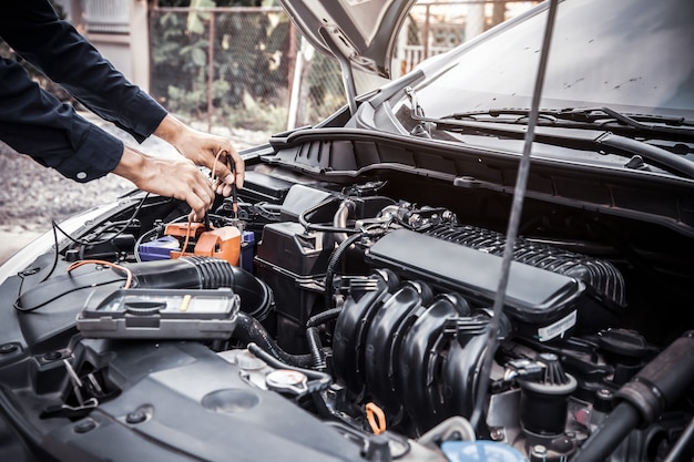 Mecánico de automóviles con herramienta de equipo de medición para comprobar la batería del coche.