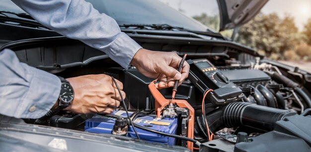 Mecánico de automóviles con herramienta de equipo de medición para comprobar la batería del coche.