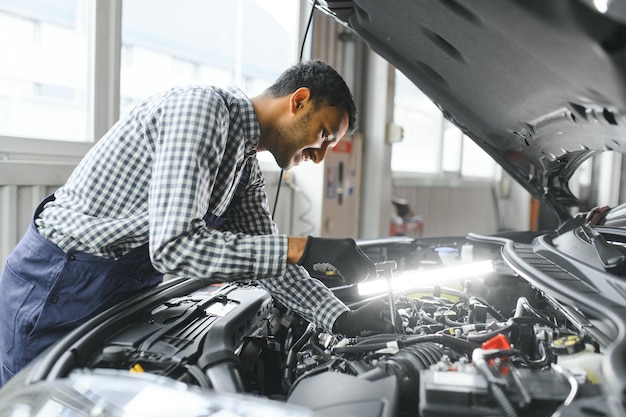 Mecánico de automóviles hispano latino en uniforme está examinando un automóvil mientras trabaja en el servicio de automóviles