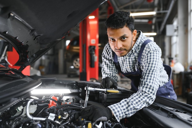 Mecánico de automóviles hispano latino en uniforme está examinando un automóvil mientras trabaja en el servicio de automóviles
