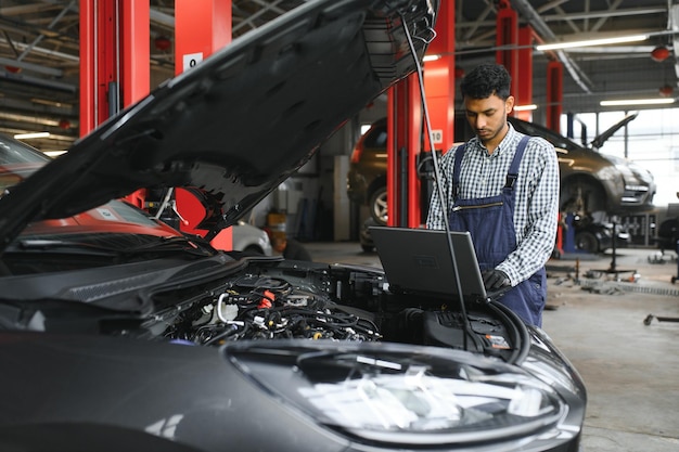 Mecánico de automóviles hispano latino en uniforme está examinando un automóvil mientras trabaja en el servicio de automóviles