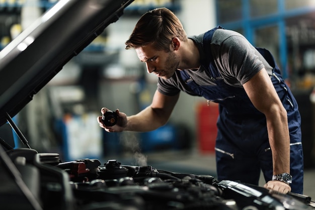 Mecánico de automóviles joven comprobando el sistema de refrigerante del coche sobrecalentado en el taller de reparación de automóviles