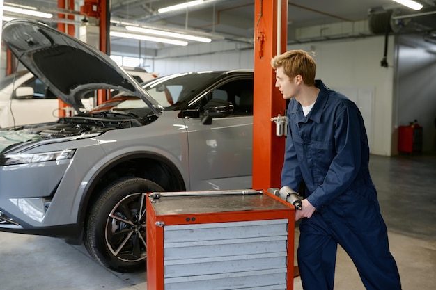 Mecánico de automóviles masculino empujando una caja de herramientas con ruedas en una estación de servicio de reparación de automóviles