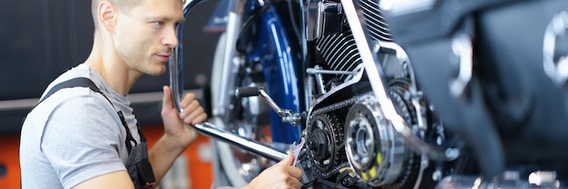 Mecánico de automóviles masculino sostiene la llave y mira el motor de la motocicleta abierta