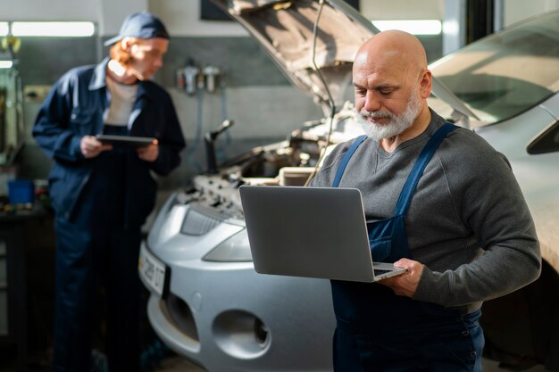 Mecánico de automóviles masculino usando un dispositivo portátil en el taller de reparación de automóviles