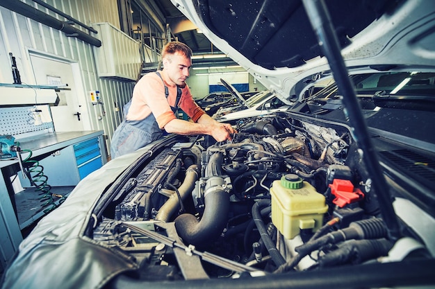 Mecánico de automóviles mirando el motor para analizar los síntomas del automóvil en la estación de servicio de reparación de mantenimiento.