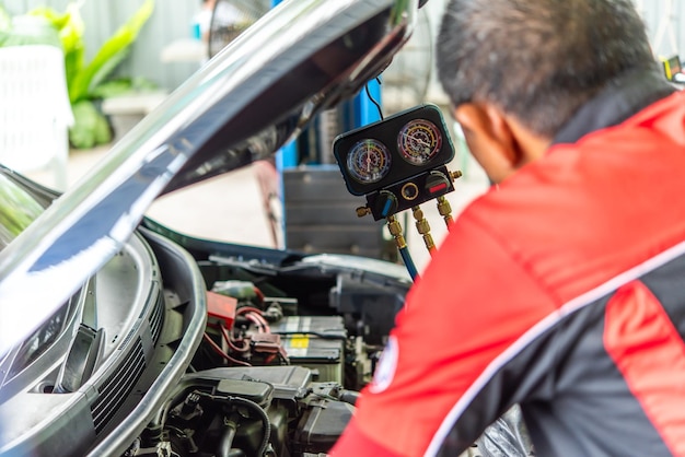 Mecánico de automóviles o técnico que rellena el aire acondicionado y comprueba un compresor de aire