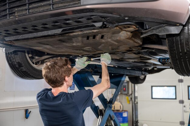 mecánico de automóviles de pie bajo el automóvil levantado y arreglando el automóvil en el garaje
