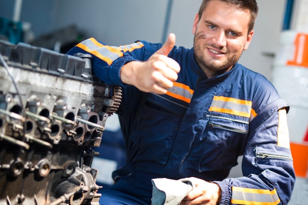 Foto mecánico de automóviles de pie junto al motor del automóvil con los pulgares para arriba.