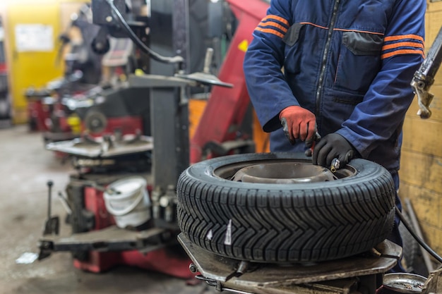 Mecánico de automóviles profesional que reemplaza el neumático en la rueda en el servicio de reparación de automóviles