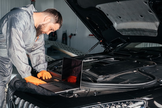 Mecánico de automóviles que trabaja con una computadora portátil en el servicio de reparación de automóviles que controla el motor del automóvil