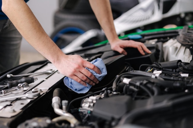 Mecánico de automóviles que trabaja en el garaje, el hombre limpia el motor del automóvil Proceso de reparación del automóvil en servicio
