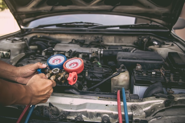 Mecánico de automóviles que utiliza la herramienta de equipo de medición para el llenado de los acondicionadores de aire de automóviles viejos.