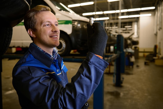 El mecánico de automóviles recoge una tuerca mientras repara un automóvil en un taller de automóviles. Concepto de mantenimiento y servicio de automóviles