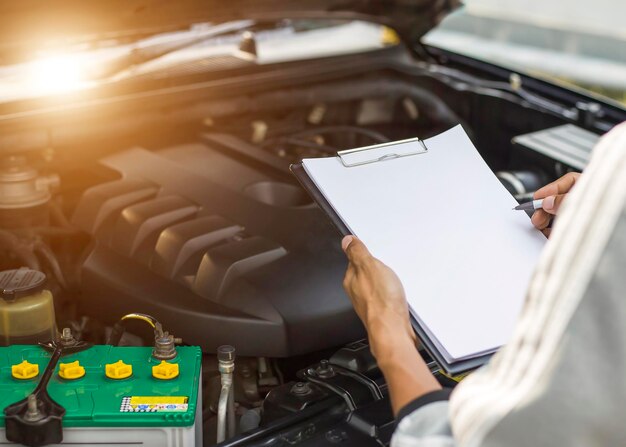 Mecánico de automóviles revisando el motor del auto con un cheque escrito en el portapapeles