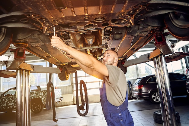 Mecánico de automóviles revisando el tren de rodaje del automóvil en la estación de servicio Trabajador masculino arreglando el problema con el automóvil Concepto de mantenimiento del vehículo