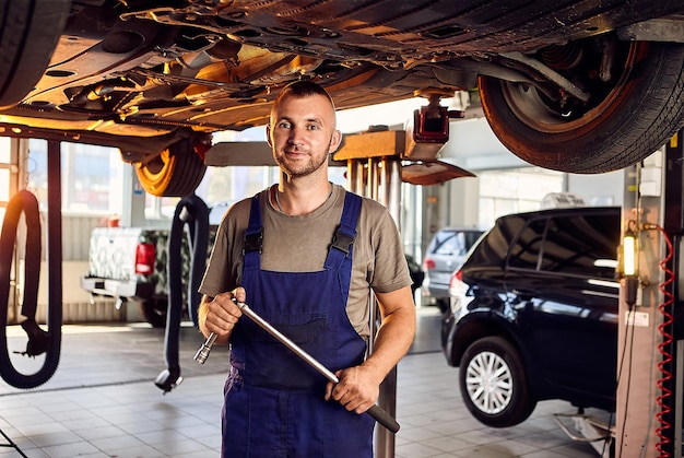 Mecánico de automóviles revisando el tren de rodaje del automóvil en la estación de servicio Trabajador masculino arreglando el problema con el automóvil Concepto de mantenimiento del vehículo