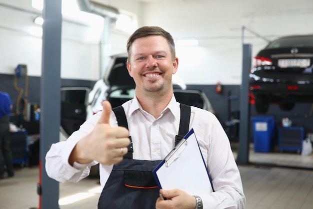 Mecánico de automóviles sonriente feliz que muestra los pulgares para arriba gesto en taller