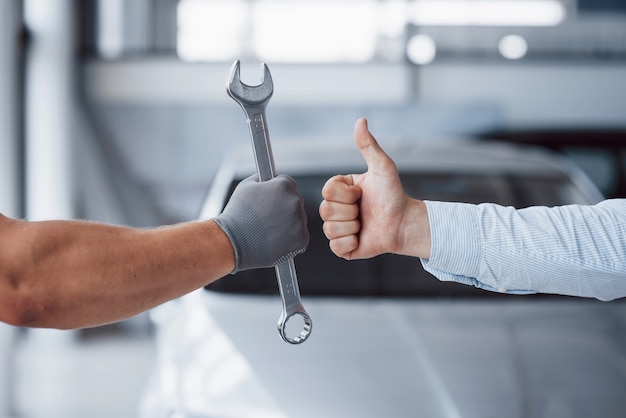 El mecánico de automóviles sostiene la llave en la mano del cliente y levanta el pulgar. Trabajo bien hecho