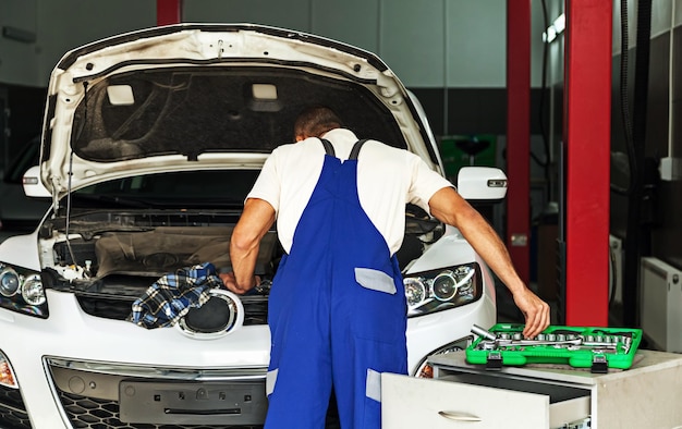 Mecánico de automóviles tomando una herramienta mientras mira el motor de un automóvil