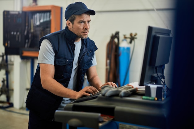 Mecánico de automóviles usando una computadora mientras trabaja en un taller de reparación de automóviles