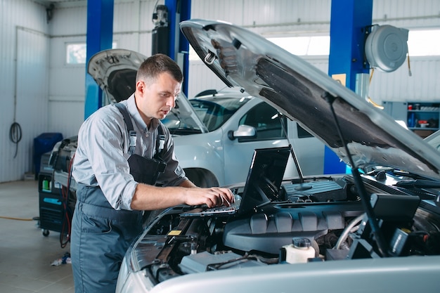 Mecánico de automóviles usando una computadora portátil para diagnosticar y verificar las piezas de los motores de los automóviles para su reparación y reparación