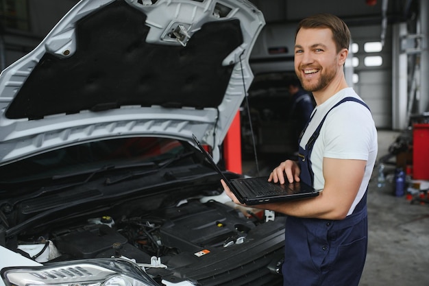 Mecánico de automóviles usando una computadora portátil para diagnosticar y verificar las piezas de los motores de los automóviles para su reparación y reparación