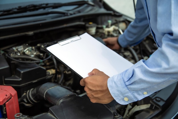 Mecánico de automóviles usando una lista de verificación en el motor del automóvil