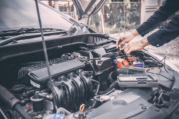 Mecánico de automóviles utilizando equipo de medición herramienta de comprobación de la batería del coche.