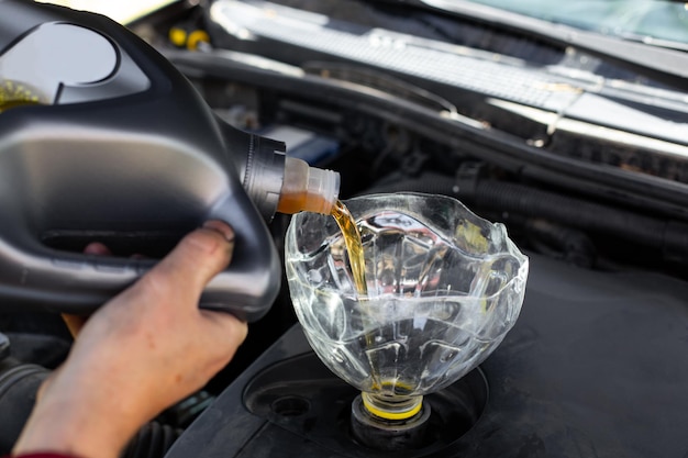 El mecánico de automóviles vierte aceite de motor en el motor del automóvil a través del embudo Cambio de aceite en el automóvil