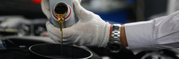 El mecánico de automóviles vierte aceite de motor en el primer plano del motor del automóvil