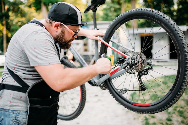 Mecánico de bicicletas en delantal ajusta con herramientas de servicio frenos de disco traseros. Taller de ciclo al aire libre