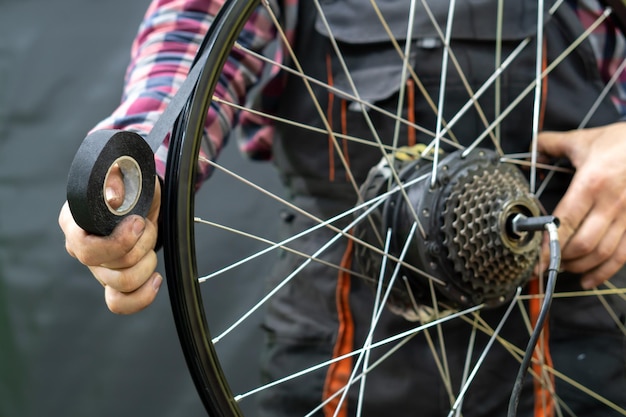 El mecánico de bicicletas sostiene en su mano la rueda trasera de la bicicleta eléctrica y la cinta de la llanta Protección de la cámara de la bicicleta contra pinchazos, cortes y fricción Reparación profesional de bicicletas