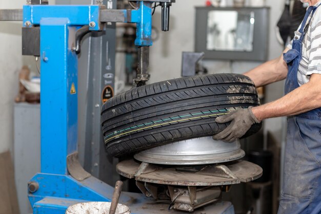 Mecánico cambiando neumáticos en el servicio de automóviles Máquina de rotación de neumáticos Mecánico de automóviles monta neumáticos en la rueda en un taller